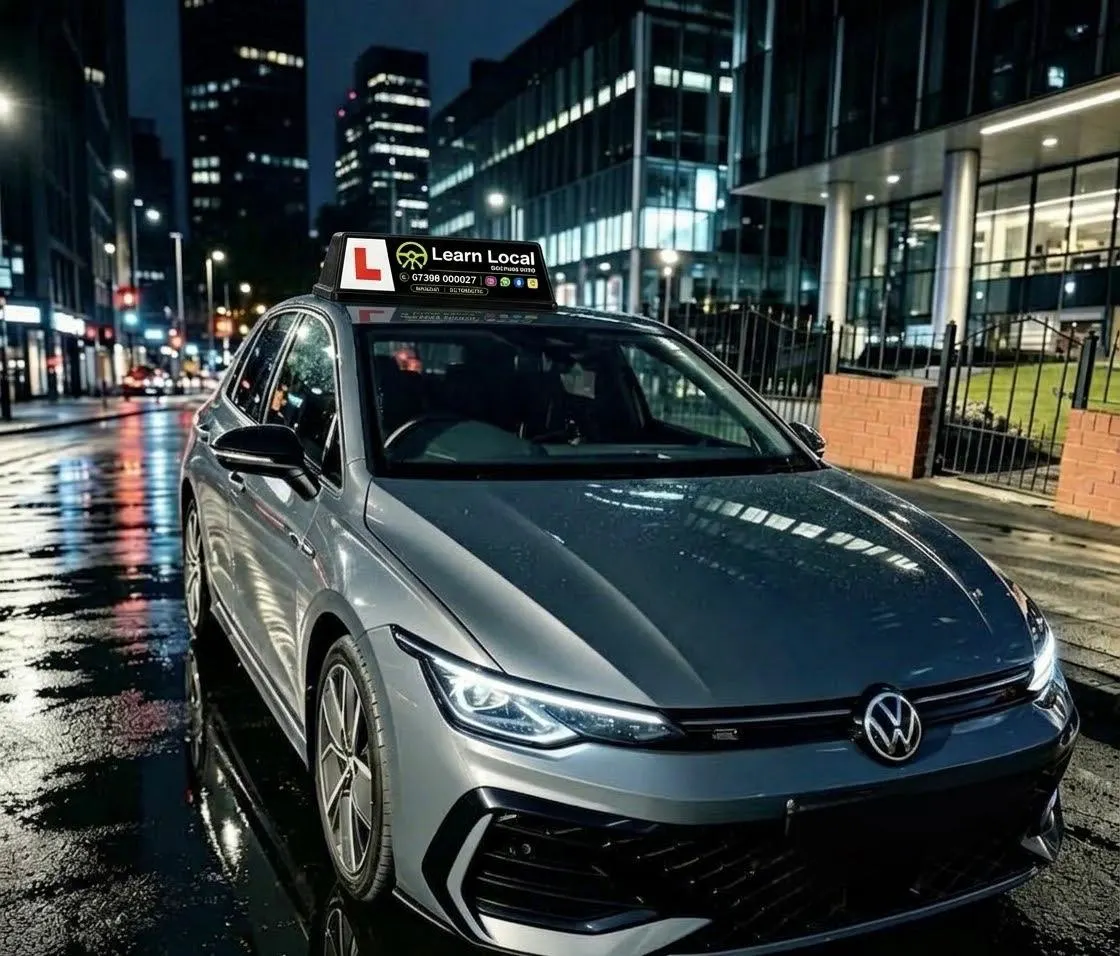 A Learn Local driving-school car with its branded roof sign on a Manchester street at night